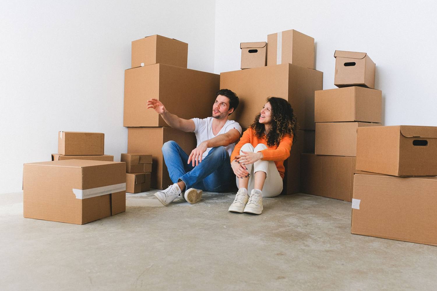 Jeune couple assis parmi des cartons dans leur nouvelle maison, prenant une pause pendant le déménagement.